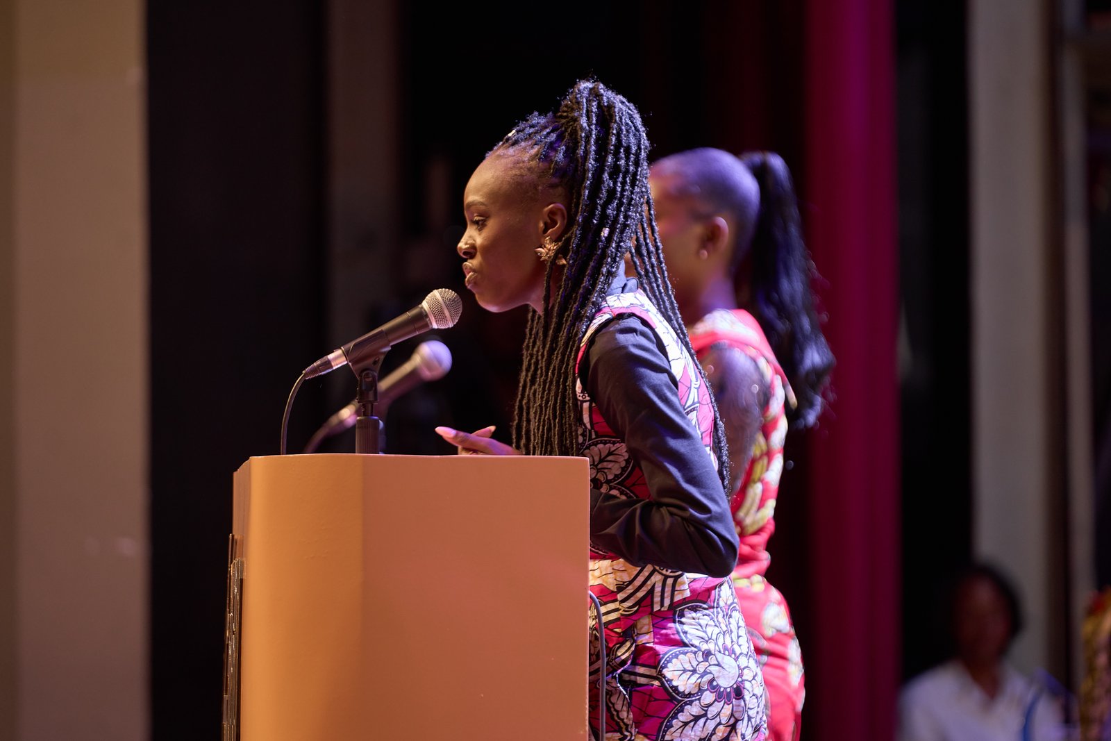 Une oratrice au pupitre face au public d’Éloquence au Féminin.