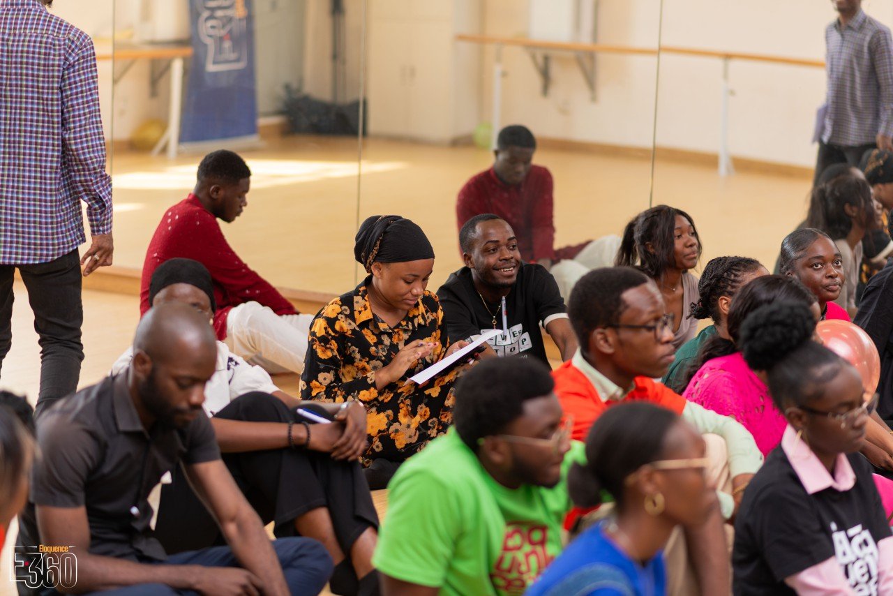Des participants assis au sol écrivent dans leurs carnets ou relisent leurs notes.